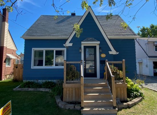 Blue cottage style house with front steps, wooden railing, and small porch
