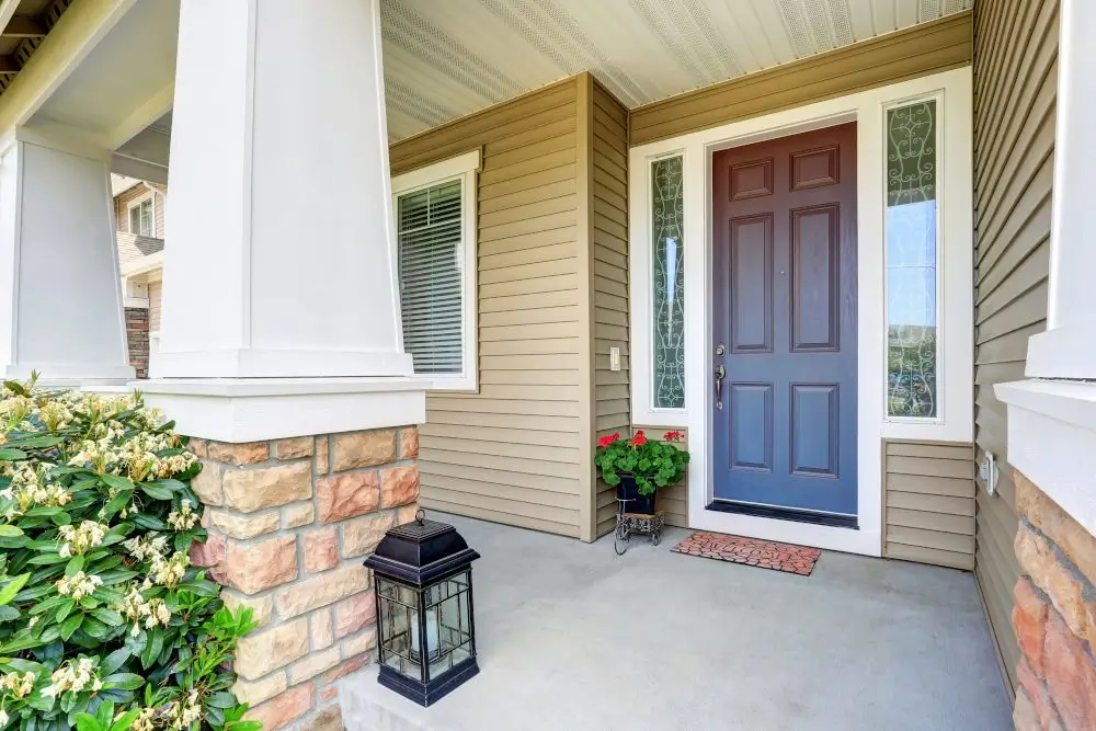 Covered front porch with blue door, stone columns, and decorative sidelights