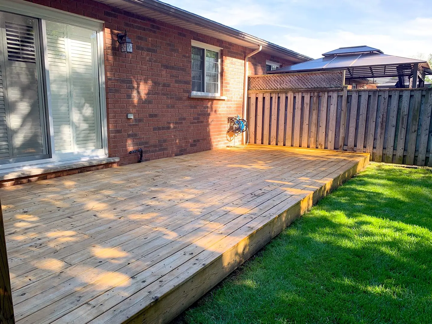 Backyard wooden deck attached to brick house with fenced lawn area