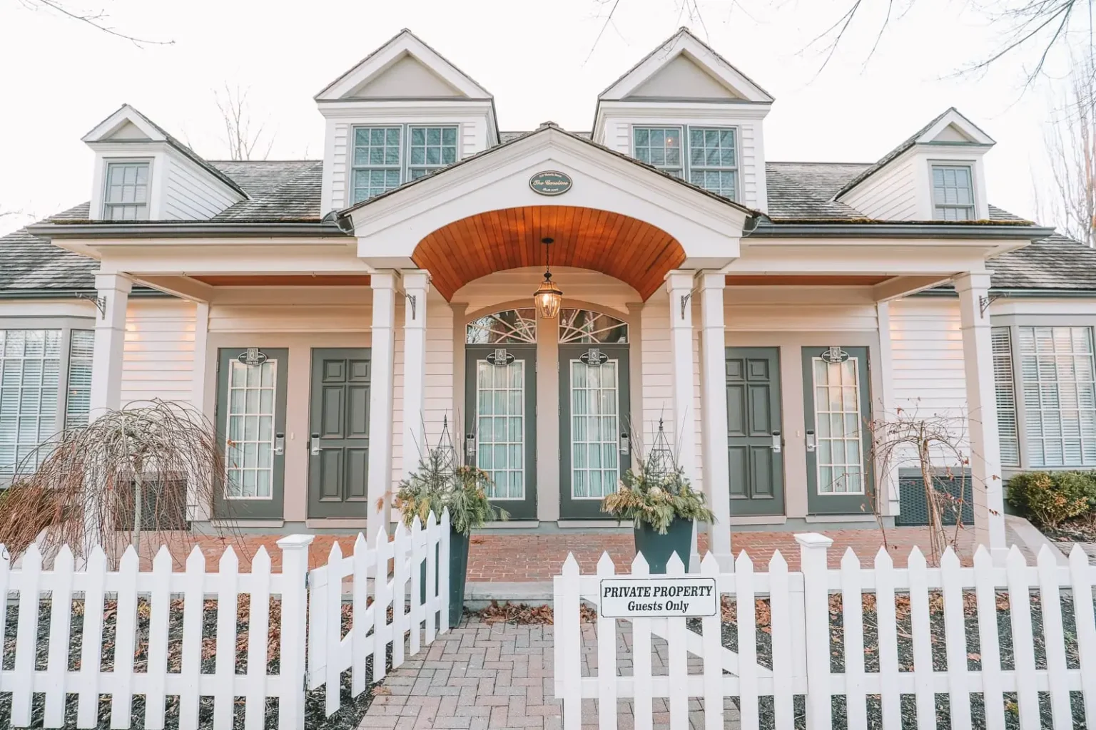 Symmetrical white cottage with dormer windows, front porch, and picket fence