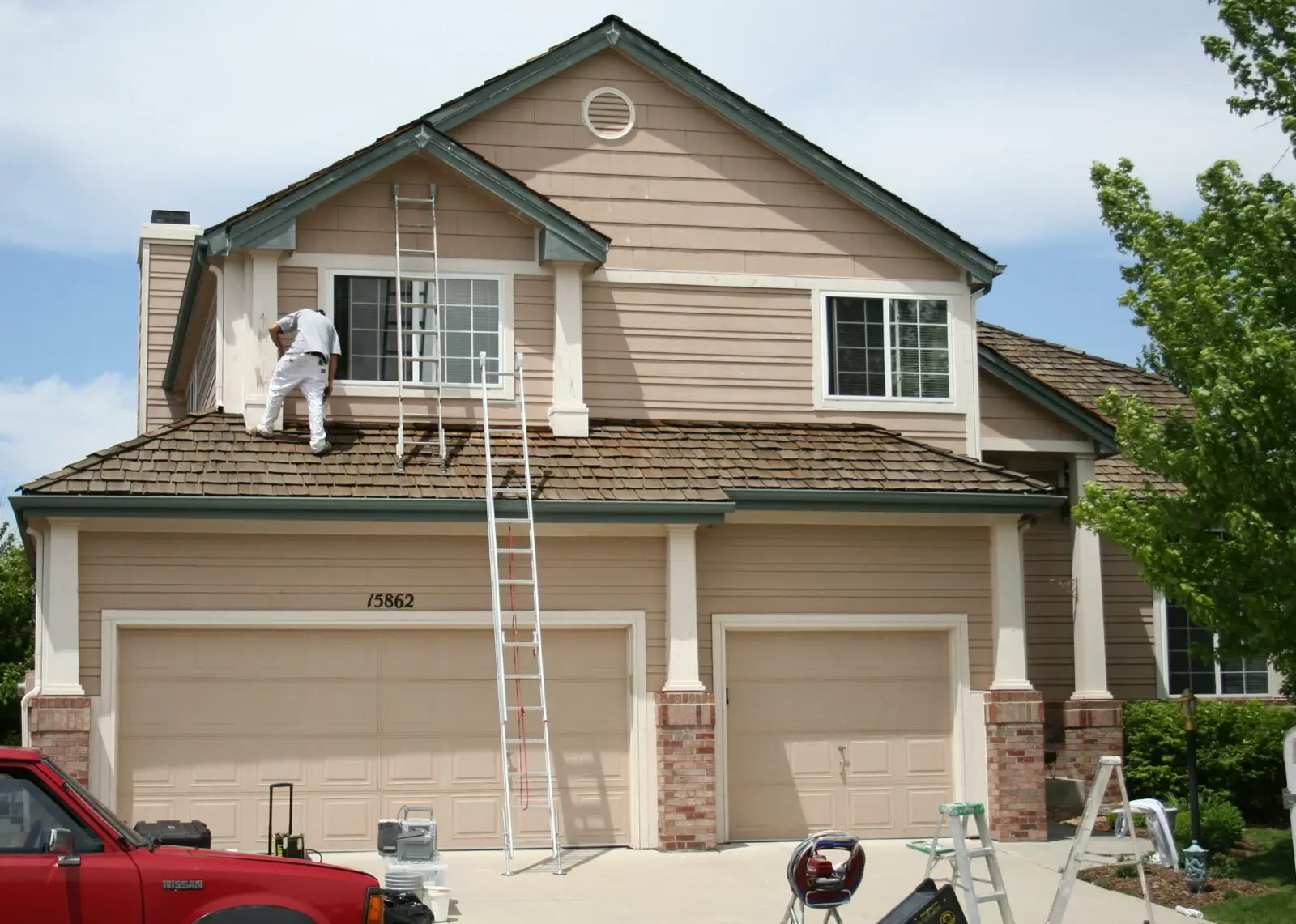 Two story suburban house exterior with painter working on roof