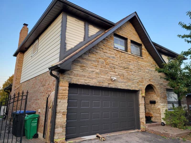 Stone and brick house exterior with black garage door and gabled roof