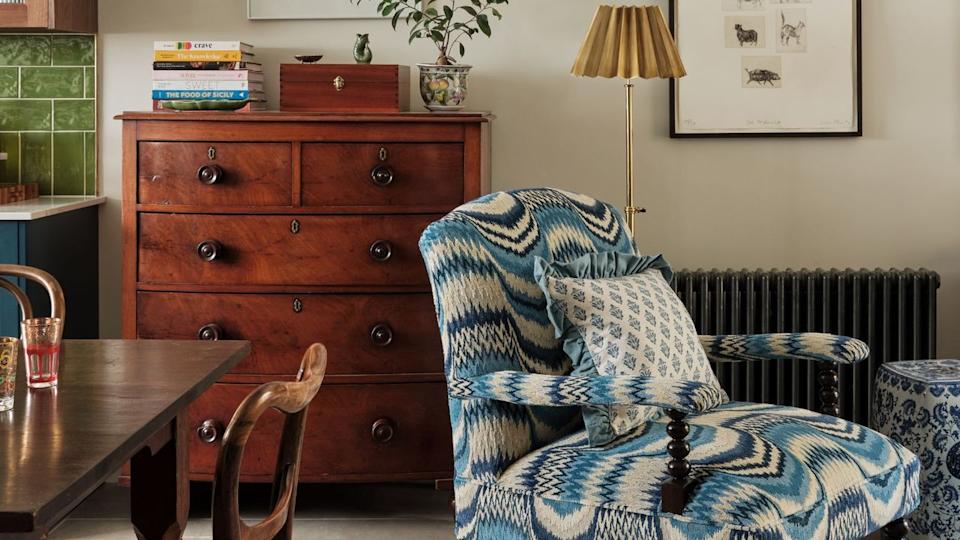 Cozy sitting area with patterned armchair, wooden dresser, and warm decor